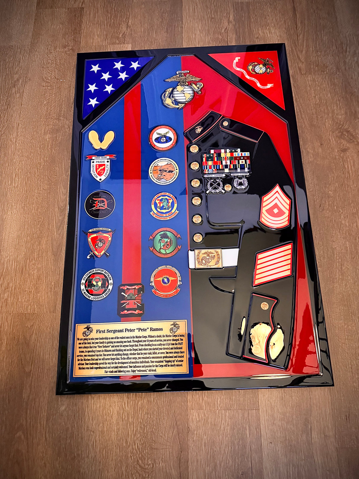 Framed military uniform display with various insignias and a flag on a wooden surface
